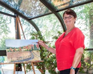 Debbie Black in her glassed-in studio makes a few changes to a painting of the driveway to her rural house.