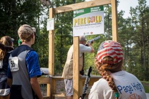 Youth look on as their fellow competitor takes aim at a sporting clays station.